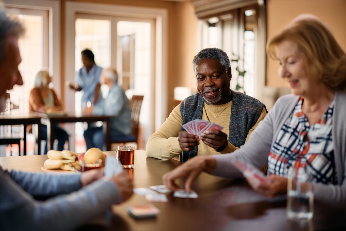 Happy African American mature man and his friends playing poker at retirement community center