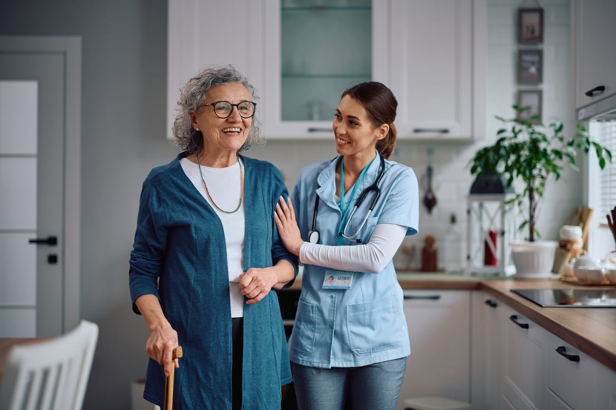 African American caregiver assisting senior patient walking through kitchen