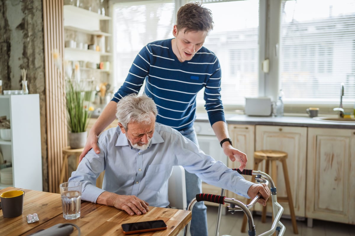 Young caregiver providing support to a senior African American man with a mobility walker in home kitchen